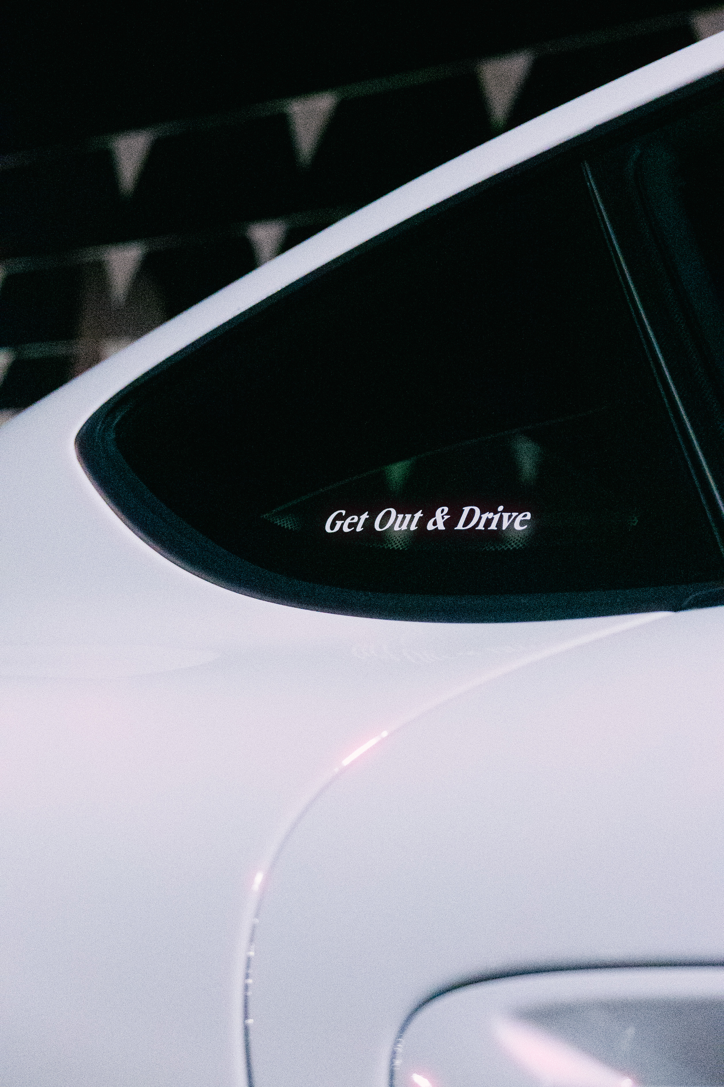 Clickable image. Rear window of white coupe with a decal that says Get Out and Drive