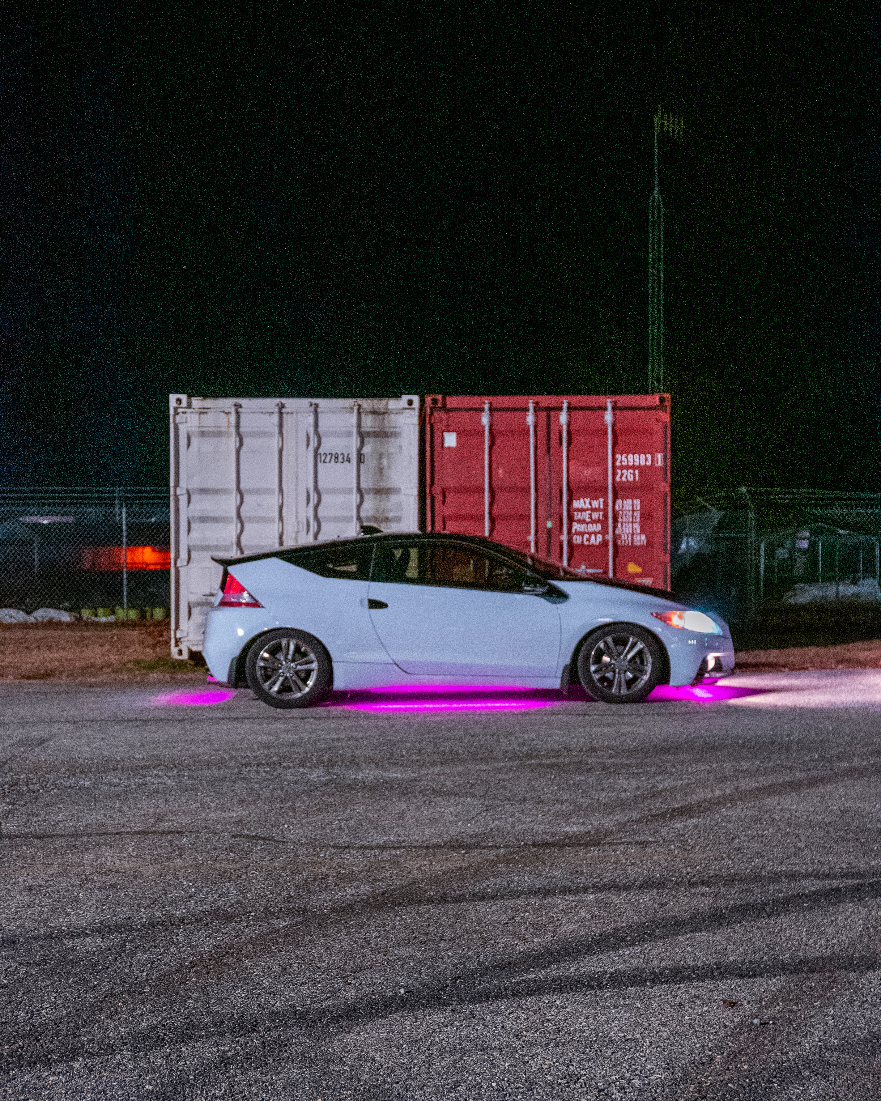 light blue hatchback in front of shipping containers